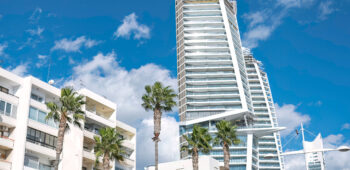 Modern skyscraper is being built, towering over traditional buildings with palm trees in Limassol, Cyprus